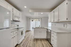 Kitchen featuring a peninsula, white appliances, white cabinets, and light countertops