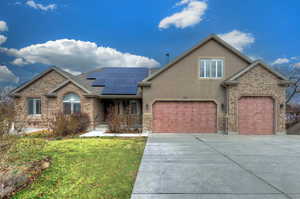 View of front facade featuring roof mounted solar panels, driveway, a front yard, brick siding, and stucco siding