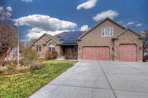 View of front facade featuring roof mounted solar panels, concrete driveway, a porch, brick siding, and stucco siding