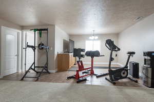 Workout room with a textured ceiling, a chandelier, and light tile patterned floors