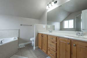 Bathroom with double vanity, light tile patterned floors, a garden tub, vaulted ceiling, and a stall shower