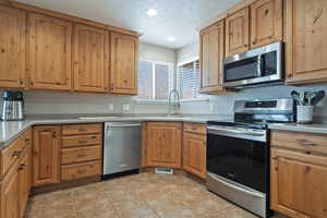 Kitchen with stainless steel appliances, a textured ceiling, recessed lighting, light tile patterned floors, and wood finish cabinets