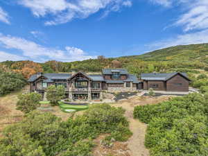 Back of property with a chimney, stone siding, a balcony, and a wooded view