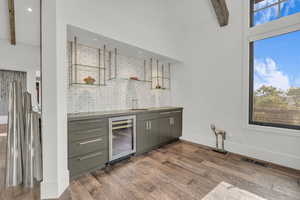 Indoor wet bar with beamed ceiling, beverage cooler, dark wood-style floors, open shelves, and gray cabinets