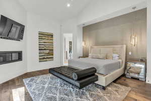 Bedroom with hardwood / wood-style flooring, recessed lighting, lofted ceiling, an accent wall, and a glass covered fireplace