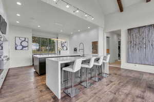 Kitchen with light stone countertops, a breakfast bar, dark wood-style floors, track lighting, and white cabinetry