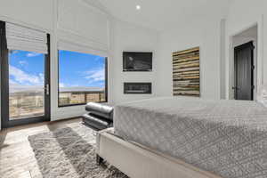 Bedroom featuring a glass covered fireplace, wood finished floors, access to exterior, recessed lighting, and vaulted ceiling