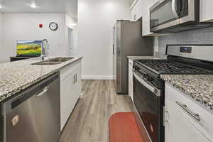 Kitchen featuring stainless steel appliances, light stone countertops, light wood-style flooring, white cabinetry, and tasteful backsplash