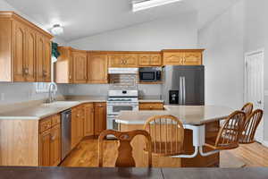 Kitchen with light wood-type flooring, stainless steel appliances, lofted ceiling, a center island, and a breakfast bar