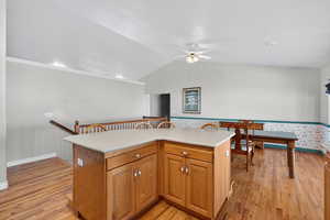 Kitchen with light countertops, a kitchen island, wood finish cabinets, and light wood-style flooring