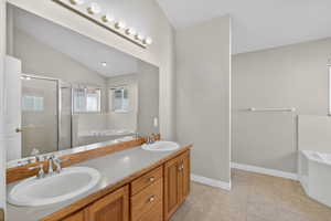 Bathroom with a garden tub, lofted ceiling, double vanity, and a stall shower