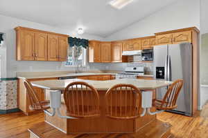 Kitchen featuring stainless steel fridge with ice dispenser, a kitchen breakfast bar, a kitchen island, gas range gas stove, and lofted ceiling