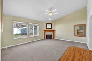 Unfurnished living room featuring hardwood / wood-style floors, a ceiling fan, lofted ceiling, a fireplace, and carpet