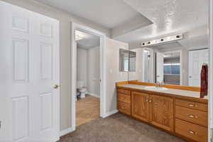 Full bath featuring vanity, a textured ceiling, and dark colored carpet
