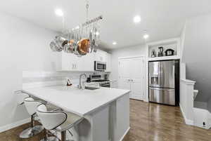 Kitchen featuring a kitchen bar, stainless steel appliances, a peninsula, dark wood-style floors, and white cabinetry