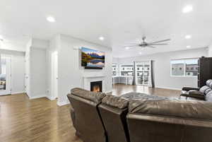 Living area with dark wood-style flooring, a glass covered fireplace, ceiling fan, and recessed lighting