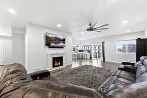 Living area with a lit fireplace, wood finished floors, ceiling fan, and recessed lighting