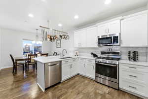 Kitchen featuring stainless steel appliances, white cabinetry, a peninsula, and dark wood-style floors