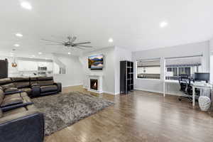 Living area with an office area, a warm lit fireplace, dark wood-type flooring, ceiling fan, and recessed lighting