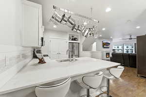 Kitchen with a breakfast bar, a peninsula, a warm lit fireplace, light stone counters, and white cabinets