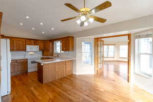 Kitchen with light countertops, wood finish cabinets, white appliances, a peninsula, and lofted ceiling