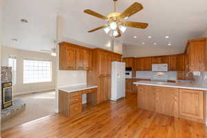Kitchen with a peninsula, light countertops, wood finish cabinetry, a ceiling fan, and white appliances
