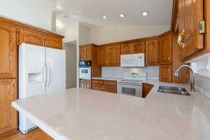 Kitchen featuring wood finish cabinets, white appliances, vaulted ceiling, a peninsula, and light counters