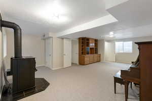 Basement with light carpet and a wood stove. Piano included with home