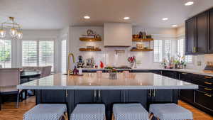 Kitchen with exhaust hood, light stone countertops, a kitchen breakfast bar, open shelves, and light wood-style flooring
