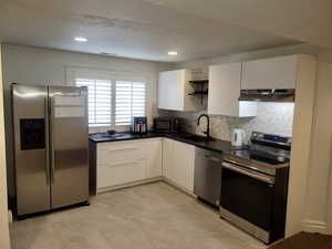Kitchen featuring stainless steel appliances, dark countertops, white cabinetry, decorative backsplash, and recessed lighting