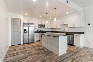 Kitchen featuring stainless steel appliances, dark countertops, a kitchen island, and white cabinets