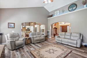 Living area with arched walkways, a ceiling fan, wood finished floors, and vaulted ceiling