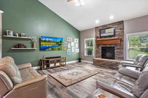 Living area with wood finished floors, ceiling fan, vaulted ceiling, and a fireplace