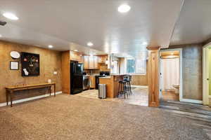Kitchen with wallpapered walls, black appliances, light countertops, a kitchen breakfast bar, and recessed lighting