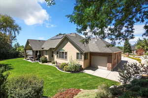 Rear view of house featuring roof mounted solar panels, a yard, an attached garage, a shingled roof, and stucco siding