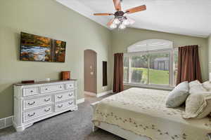 Bedroom featuring dark colored carpet, arched walkways, vaulted ceiling, and ceiling fan