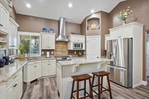 Kitchen featuring stainless steel appliances, a breakfast bar area, light stone counters, a kitchen island, and white cabinets