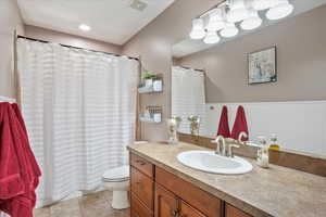 Bathroom featuring vanity, shower / bath combination with curtain, light tile patterned floors, and wainscoting