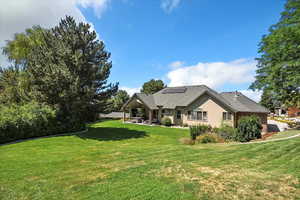 Back of house featuring a yard, a patio, solar panels, and roof with shingles