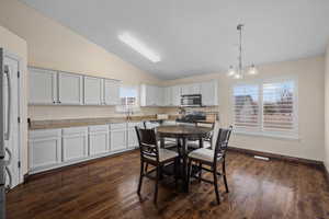 Dining area featuring vaulted ceiling, dark wood-style flooring, and hanging lights