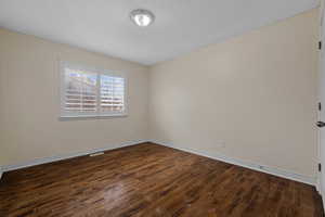 Spare room featuring dark wood-style floors and baseboards