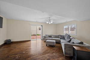 Living area featuring dark wood-style flooring, plenty of natural light, and a ceiling fan