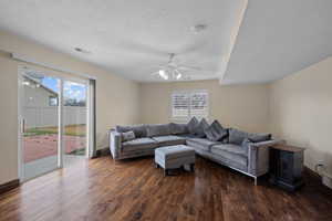 Living room with dark wood-style flooring, healthy amount of natural light, ceiling fan, and a textured ceiling