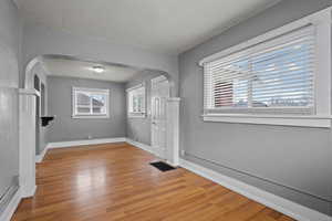 Foyer with a textured wall, arched walkways, and light wood finished floors