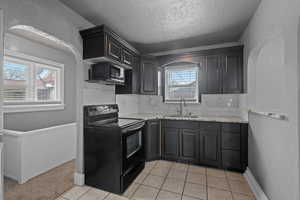 Kitchen with a textured wall, black appliances, decorative backsplash, a textured ceiling, and light stone counters