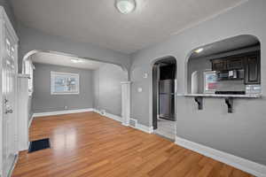 Unfurnished room with a textured wall, arched walkways, light wood finished floors, and a textured ceiling