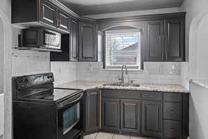 Kitchen featuring black appliances, a textured wall, light stone countertops, decorative backsplash, and light tile patterned floors