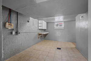 Basement with a textured wall, a textured ceiling, and light tile patterned flooring