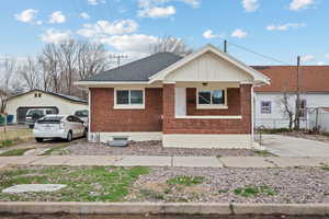 View of front of house with brick siding, covered porch, an outdoor structure, and roof with shingles