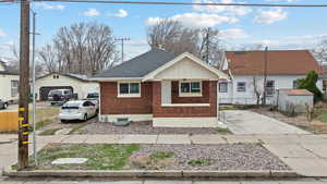 View of front facade with an outdoor structure, brick siding, roof with shingles, board and batten siding, and a porch
